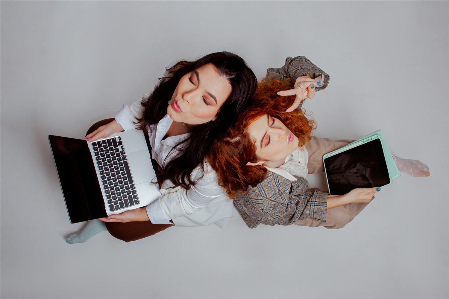 Ediane e Isadora vistas de cima, com notebook e tablet, em um momento descontraído do ensaio da Mivō